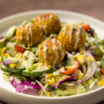 bowl of vegetables with chickpea masala patties on top with dressing drizzled over