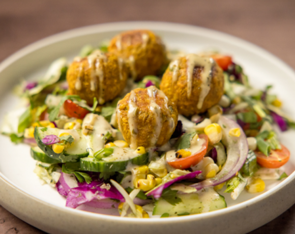 bowl of vegetables with chickpea masala patties on top with dressing drizzled over