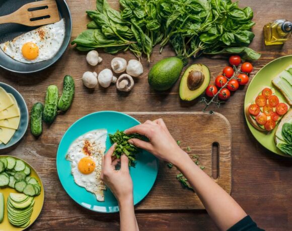 Overhead shot of hands preparing a meal over cutting boards with fresh produce and eggs in the shot